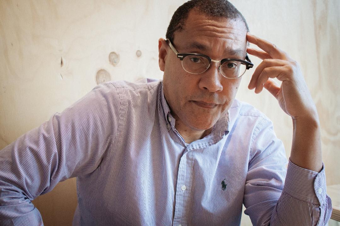 A photo of a black man with glasses in front of a neutral background